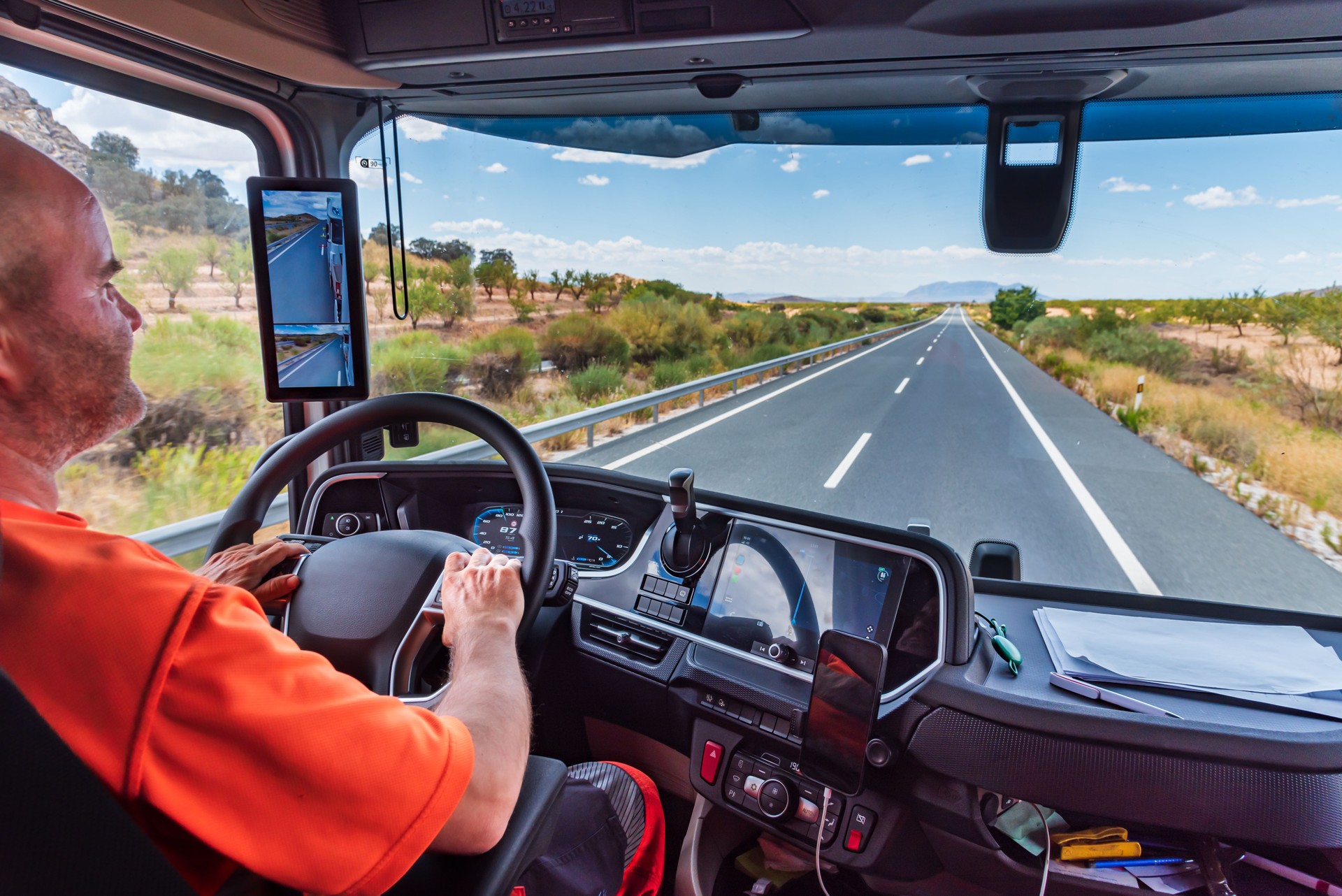 From inside the cab of a truck, driver holding the steering wheel firmly while driving on a straight highway, usually where fatigue increases the most.